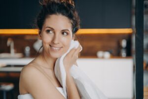 Smiling hispanic girl wiping face by towel enjoy fresh glowing skin after skincare treatment at home